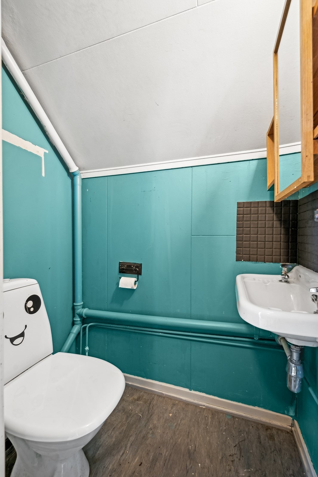 Toalettrom med malte plater og belegg på gulv. Rommet har håndvask montert på vegg og gulvmontert toalett. Galleribilde