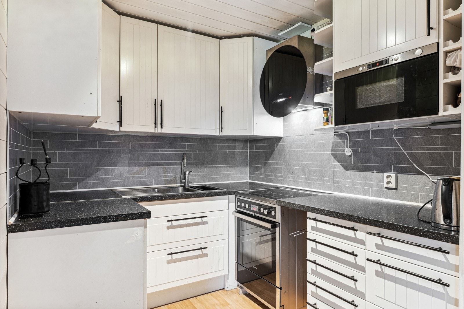 Åpen kjøkkenløsning. Kjøkkeninnredning med profilerte fronter. Plater over laminert benkeplate . Integrert mikrobølgeovn. Vegghengt ventilator med kullfilter. Galleribilde