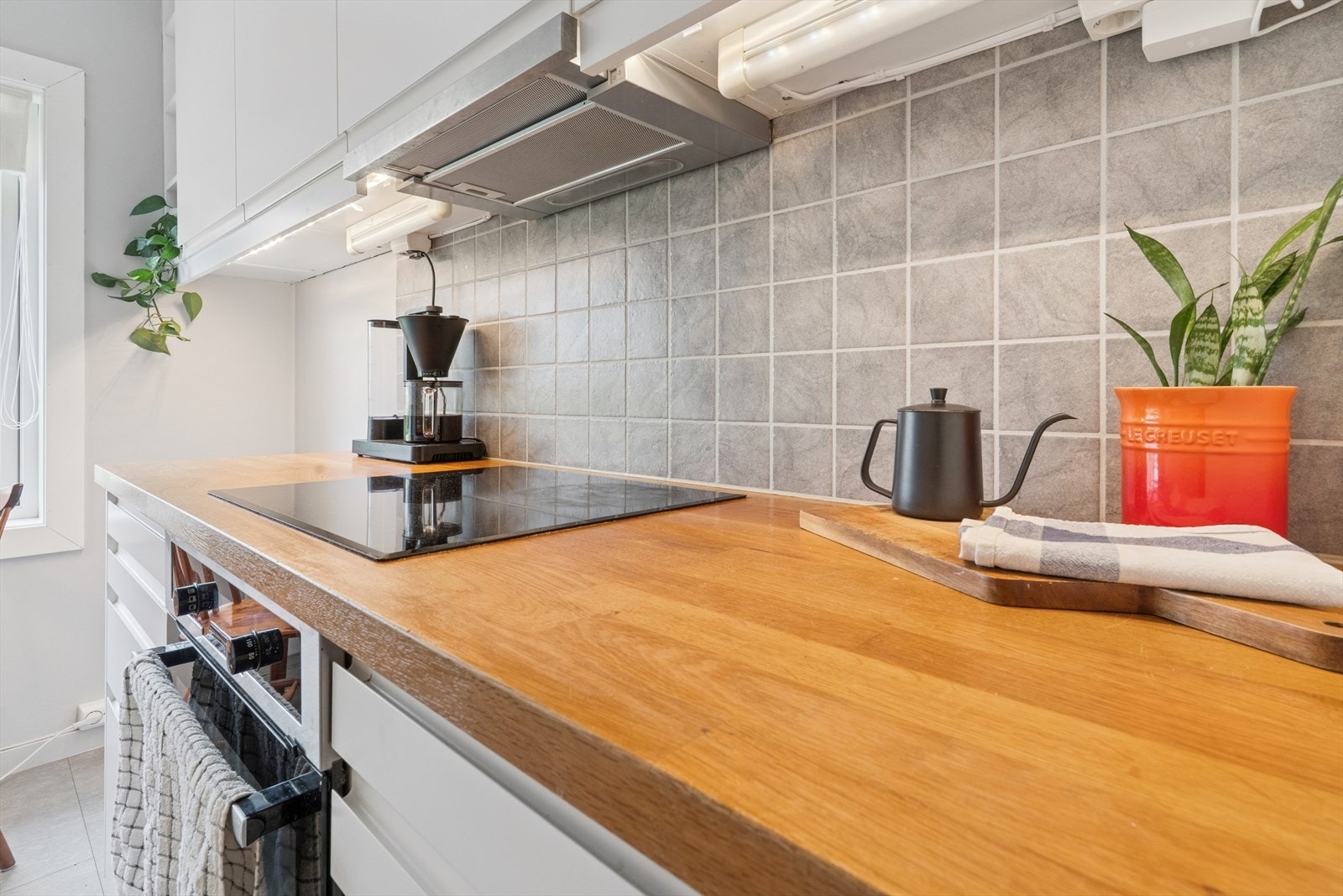 Kjøkkenet har glatte folierte fronter, benkeplate i tre med nedfelt kum i rustfritt stål, fliser på vegg over benk og ventilator tilsluttet kanal ledet ut på yttervegg. Galleribilde