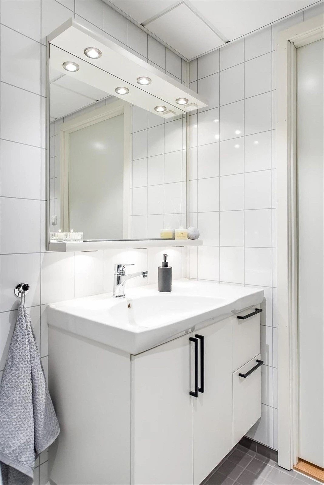 Lys baderomsinnredning med heldekkende servant og speil med belysning over. Baderommet er også utstyrt med dusjhjørne med glassdører, veggmontert toalett og opplegg for vaskemaskin. Galleribilde