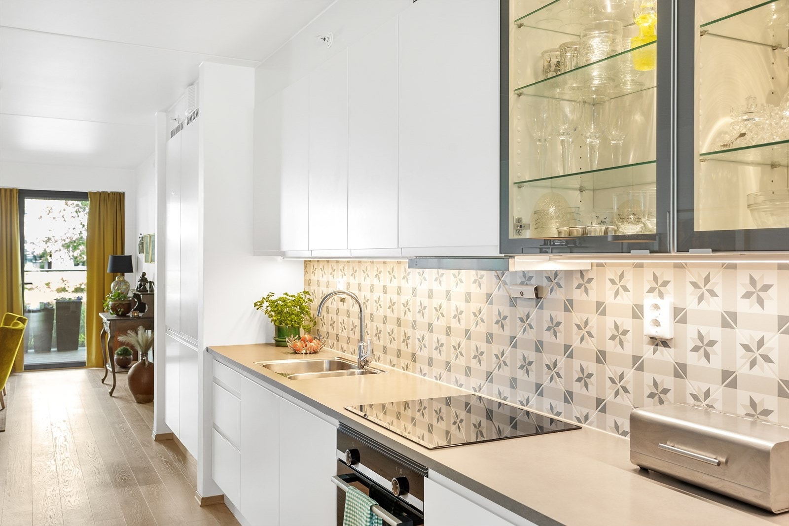 De slette overflatene og fliser over benkeplaten, samt den gjennomførte belysningen under overskapene fremhever kjøkkenets moderne estetikk. Galleribilde