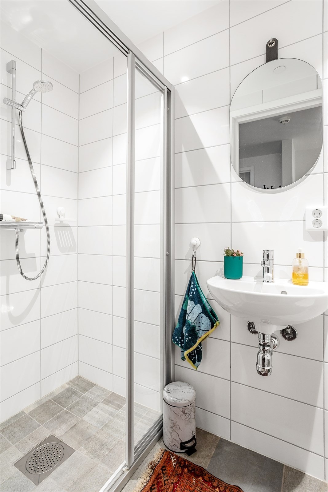 Delikat flislagt baderom med varmekabler og enkel servant, speil, dusjhjørne og vegghengt toalett. Galleribilde