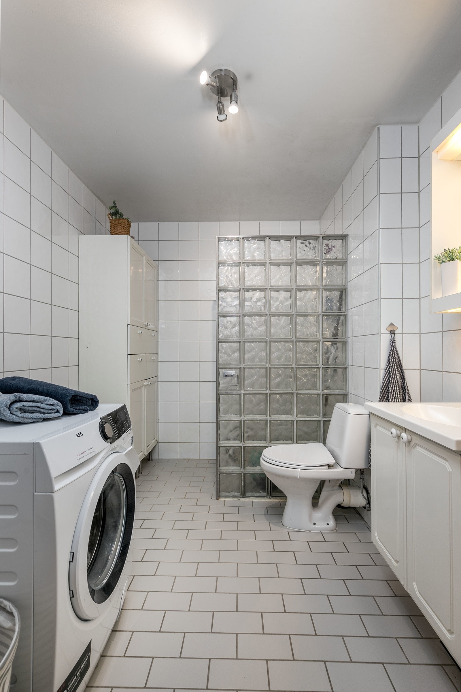 Videre har badet et separat dusjhjørne med vegg i glassbyggerstein, frittstående toalett og opplegg for vaskemaskin. Galleribilde