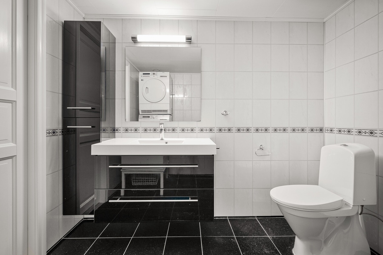Innredet med servant med skuffer under, speil med belysning, vegghengt høyskap, samt toalett og dusjhjørne med dører i aluminium. Galleribilde