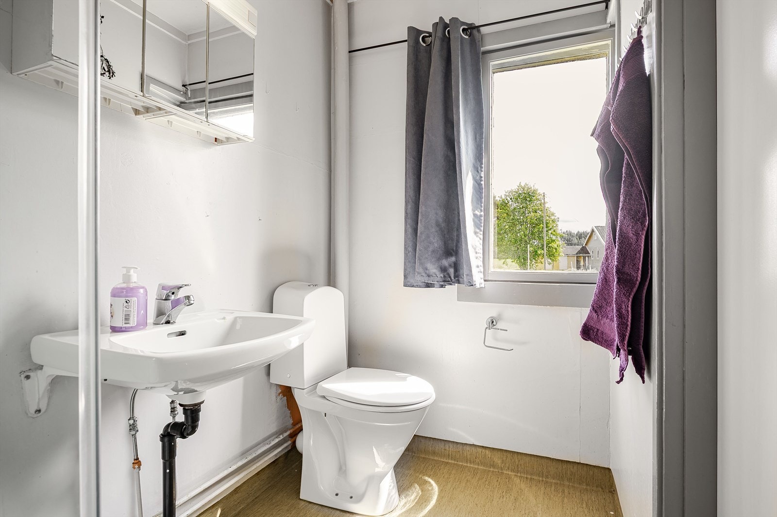 Lyst og eldre baderom med gulvbelegg med oppbrett og lysmalte plater på veggene. Galleribilde