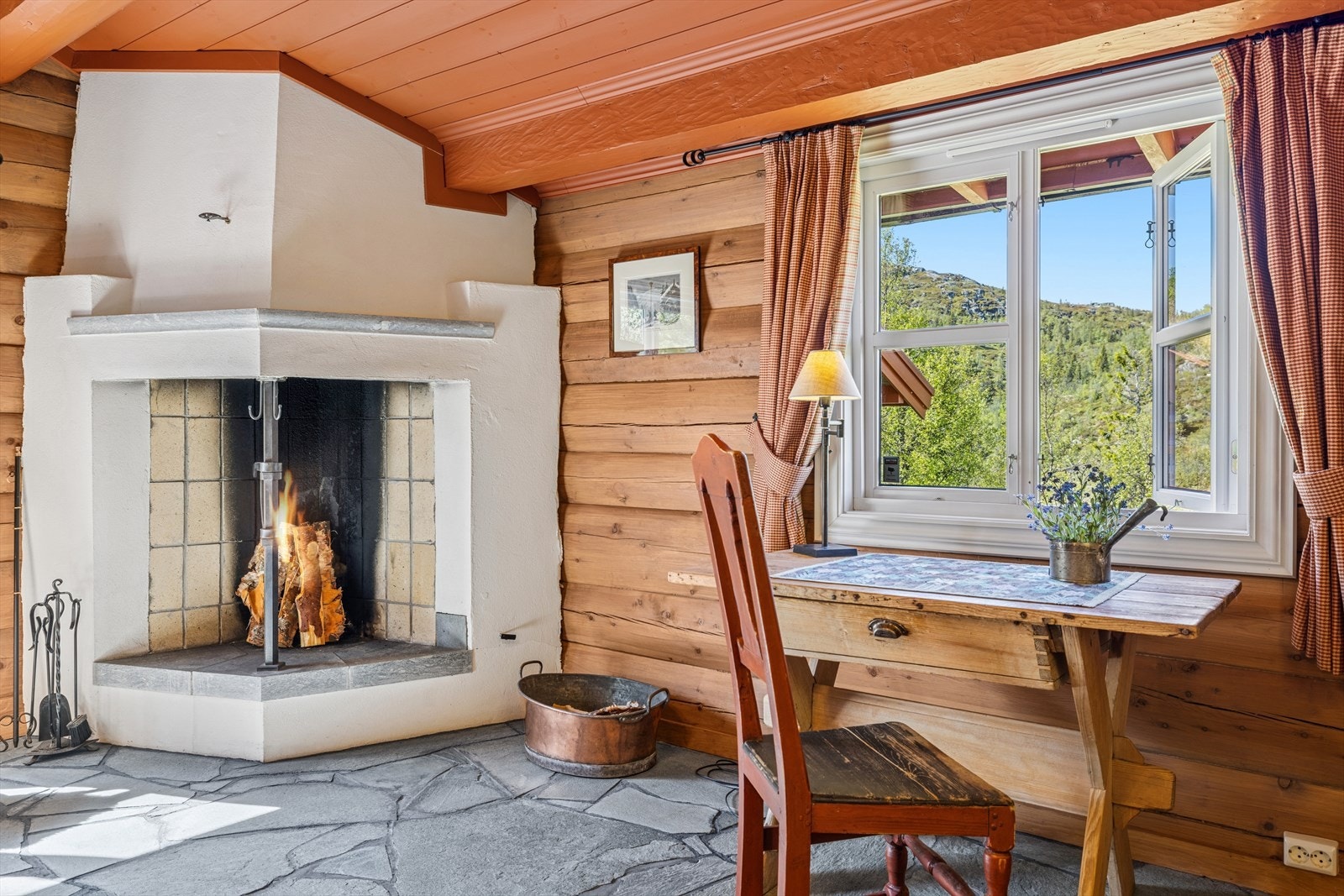 Rommet er generøst utformet, med skiferfliser og varmekabler i gulvet, laftede tømmervegger og åpen, malt himling. Den sjarmerende peisen tilfører både varme og stemning - et rom for både ro og hyttekos. Galleribilde
