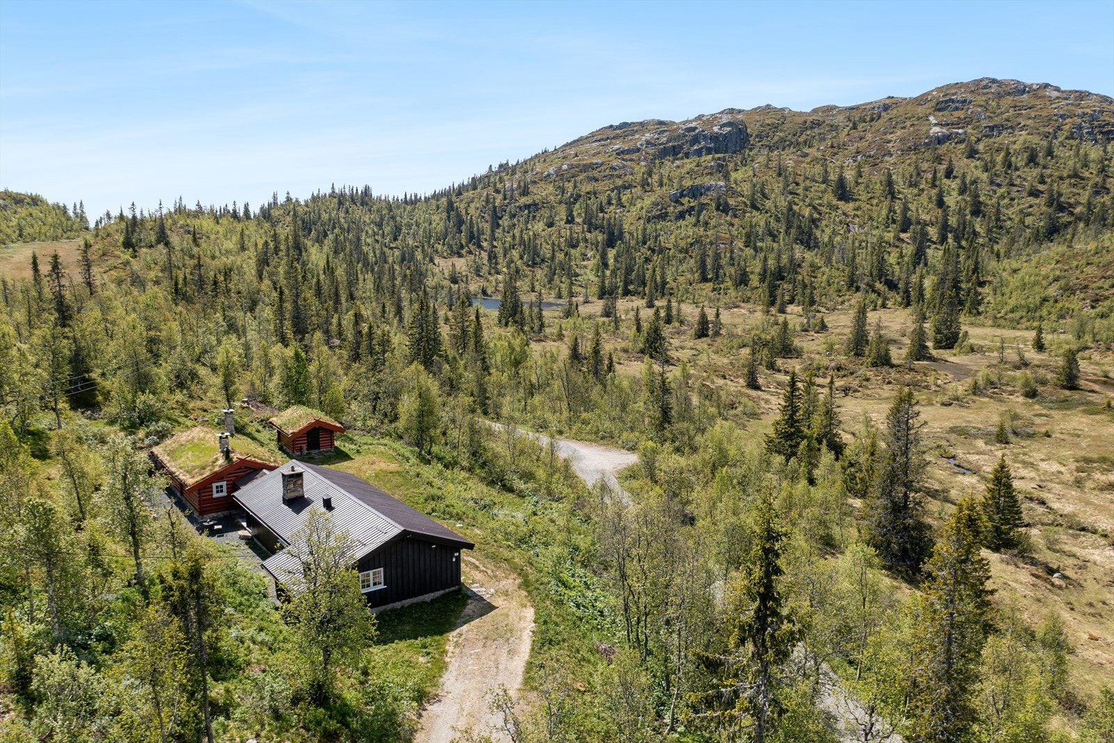I fremkant av eiendommen, på et lavere nivå, går det en vei som fører til en annen hytte lenger inn i terrenget. Foran denne veien ligger et friområde som gir ytterligere romfølelse og avstand til øvrig bebyggelse. Galleribilde