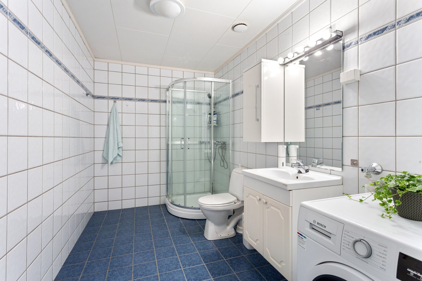 Flislagt bad med gulvvarme. Innredet vegghengt servantinnredning med dører. Speil med overlys over servant. Galleribilde