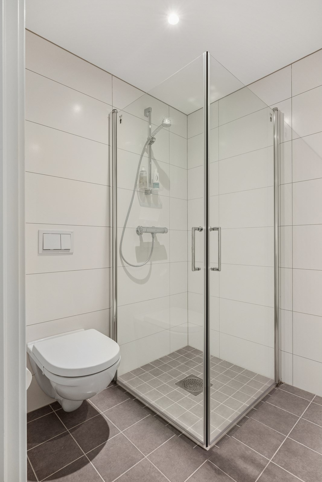 Badet har en innredning med heldekkende servant, veggmontert toalett og dusjvegger/hjørne. Galleribilde