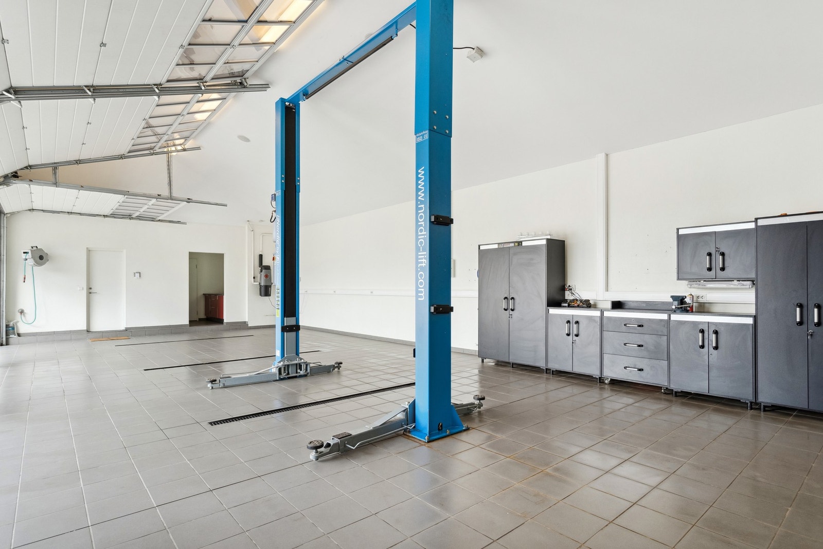 Garasjen er innredet med løftebukk, arbeidsbenk og flislagt gulv - et drømmerom for bilentusiasten eller den praktiske huseieren. Galleribilde