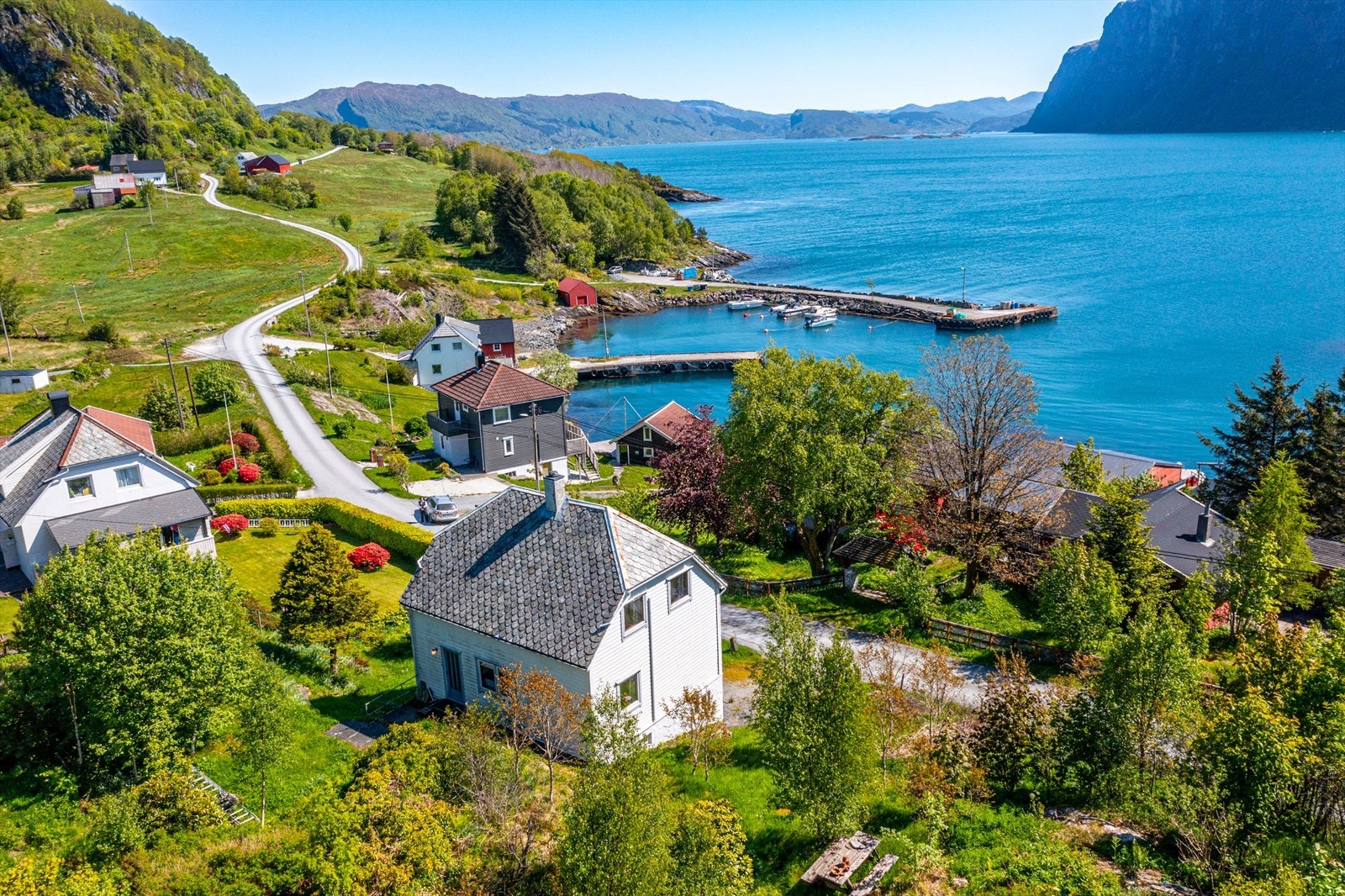 Stor tomt like ved fjorden opparbeida med grøntareal, tre, planter og ein del naturleg vegetasjon Galleribilde