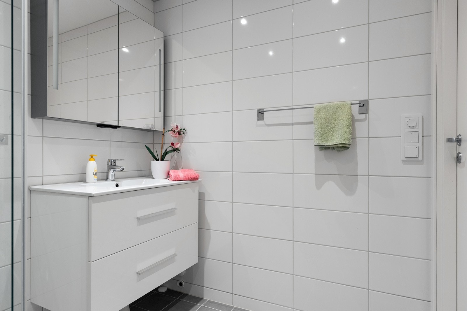 Badet ble oppgradert i 2020 og fremstår som moderne og stilrent. Det er grå fliser på gulvet med varmekabler, og veggene er kledd med hvite fliser. Rommet er innredet med hvit baderomsinnredning med skuffer, samt speilskap med integrert belysning. Galleribilde