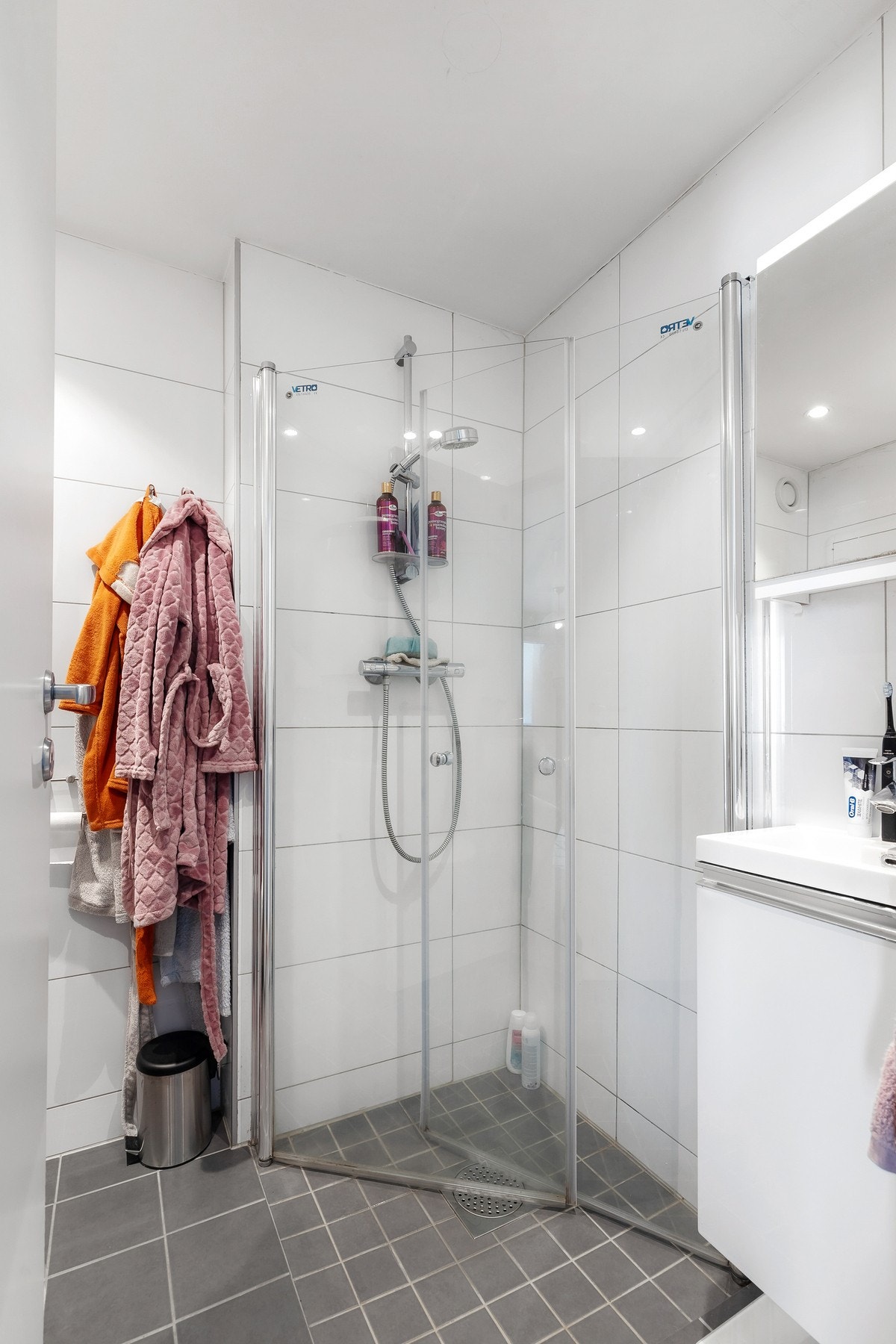 Videre er badet innredet med dusjhjørne med dører og vegghengt dusjarmatur Galleribilde