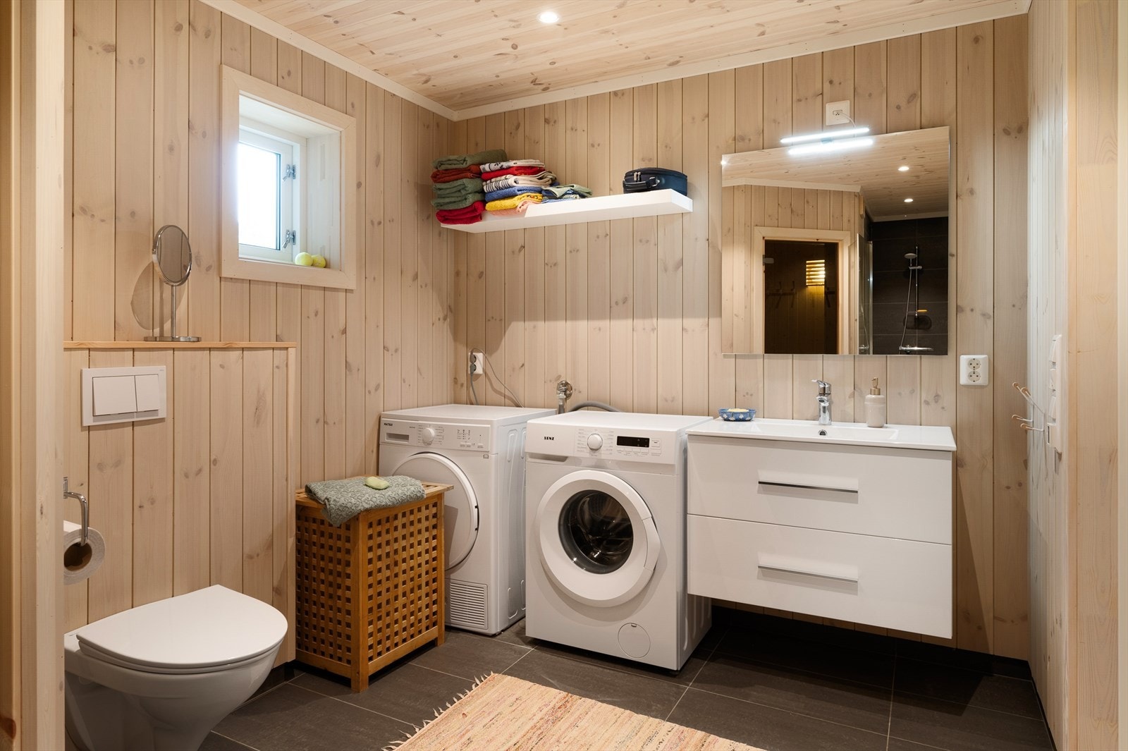 Badet har veggmontert toalett og opplegg for vaskemaskin og tørketrommel. Galleribilde