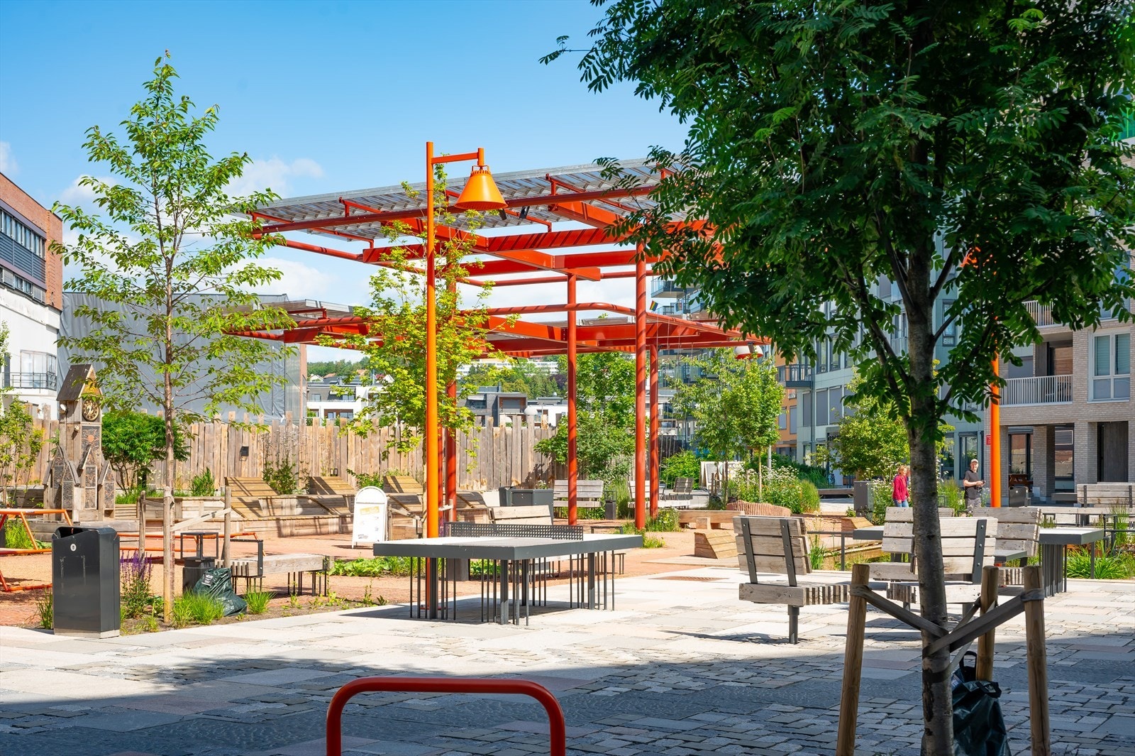 Vollebekk torg med to lunder, grusdekker og uformelle arenaer for opphold og aktivitet. I midten av torget finnes en paviljong. Galleribilde