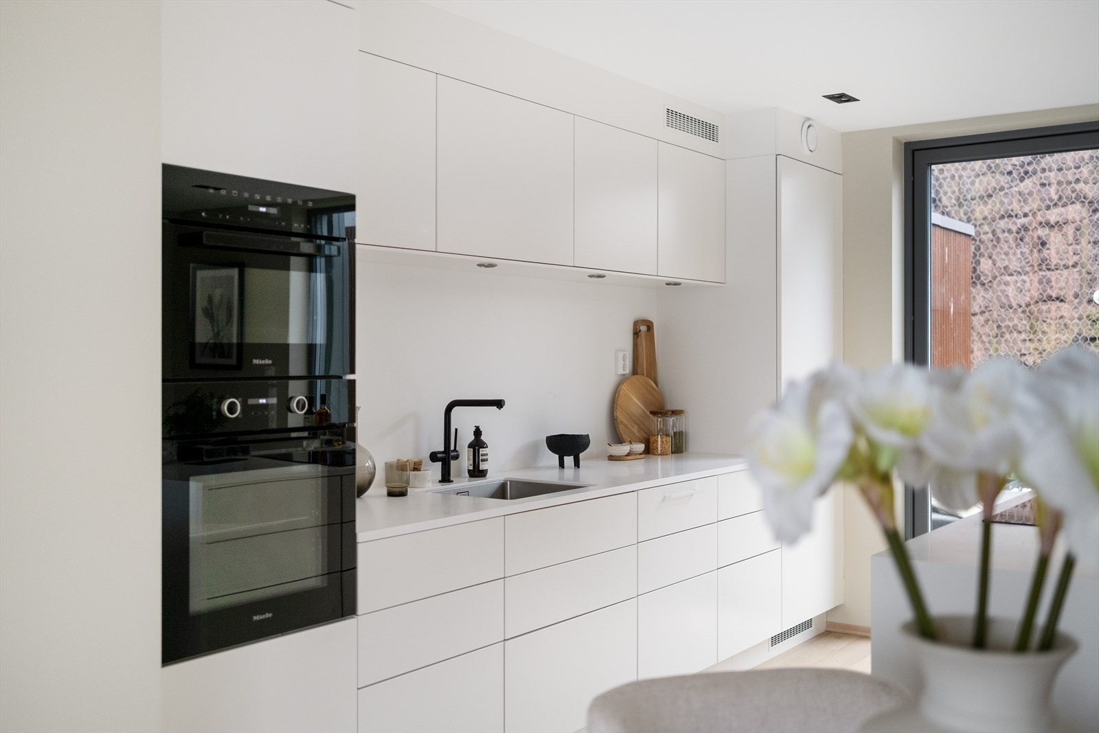 Løsningen er både praktisk og stilren, med skap og skuffer langs én vegg, samt en kjøkkenøy med barløsning og nedfelt induksjonstopp med ventilator Galleribilde