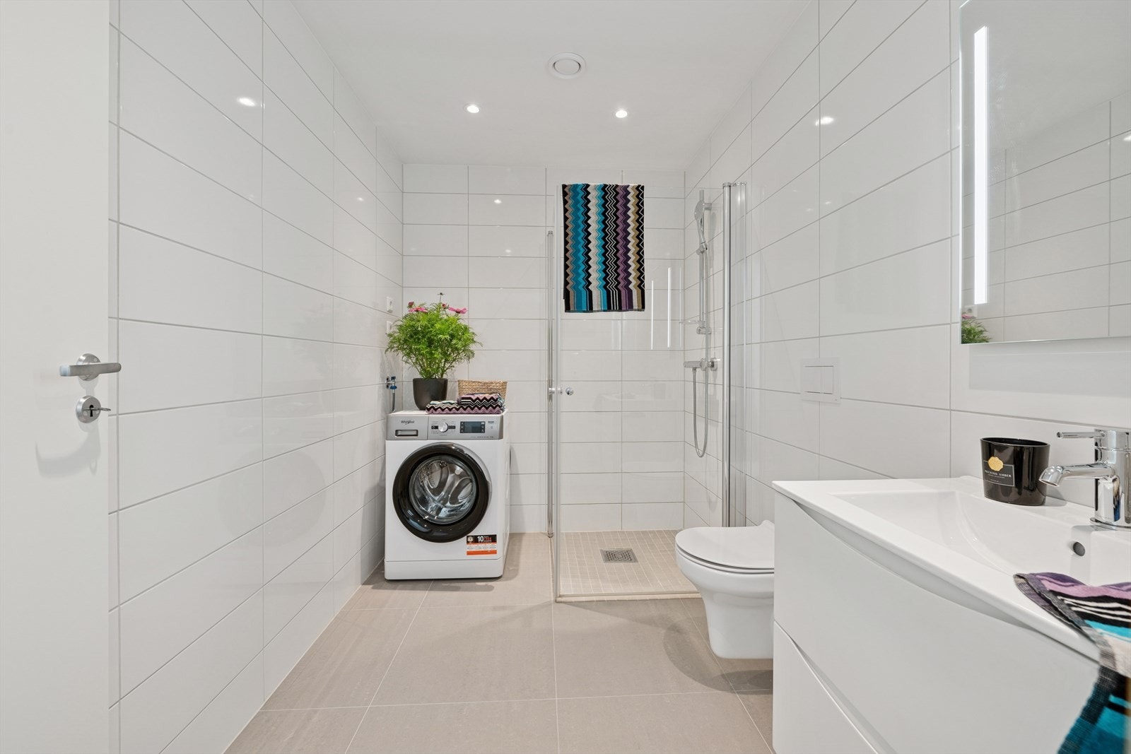 Hoved bad med fliser på gulv og vegg. Her er det også opplegg for vaskemaskin og tørketrommel. Galleribilde