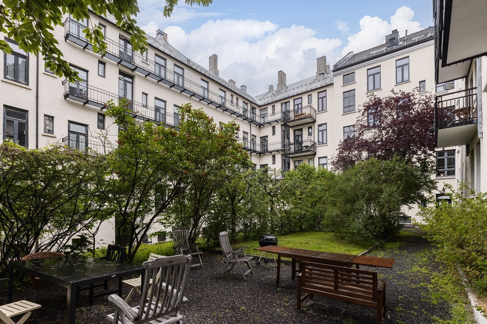 Pent opparbeidet bakgård med sittegrupper og grill, plen og beplantning. Galleribilde