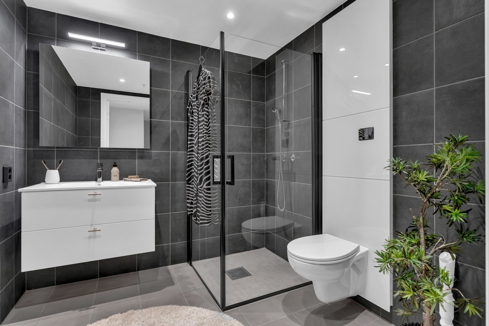 Badet er av en god og romslig størrelse hvor det er lagt delikate fliser i nydelige gråtoner. Her er det oppvarming via deilige varmekabler i guvlet. I tillegg er det avsatt plass og opplegg til både vaskemaskin og tørketrommel. Galleribilde