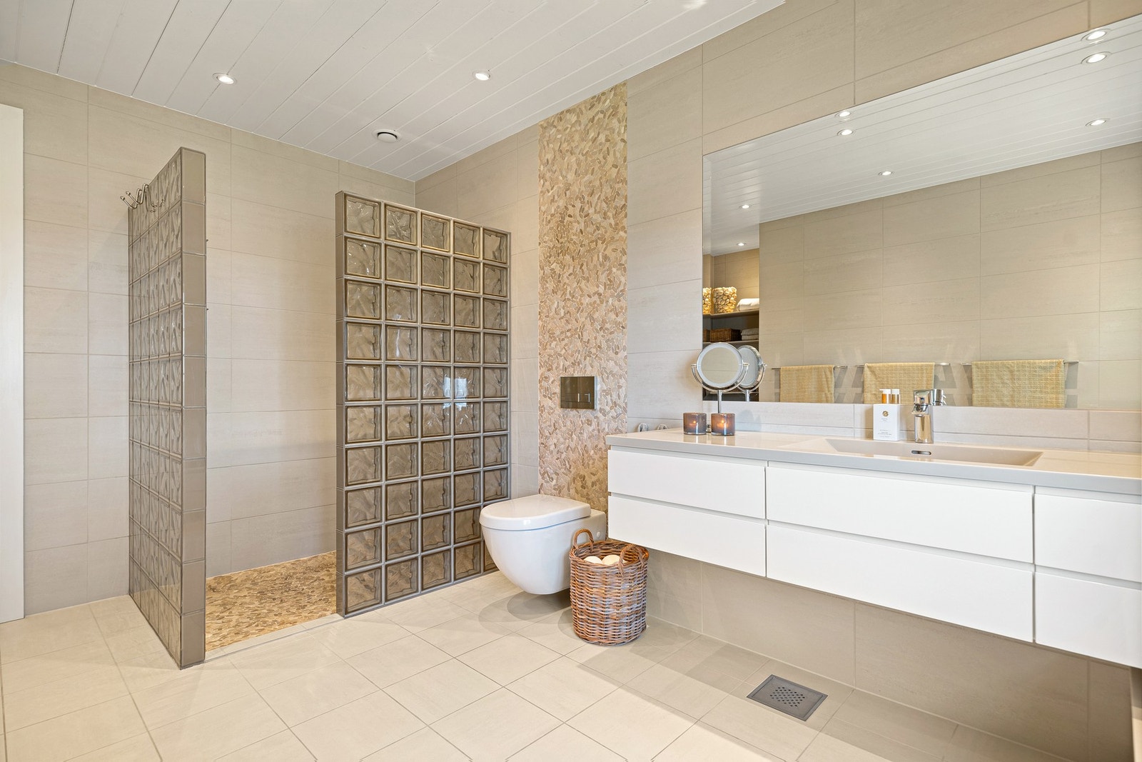 Badet er flislagt med beige fliser på gulv og vegger, downlights i taket, samt elvesteiner i dusjen og over toalettet. Galleribilde