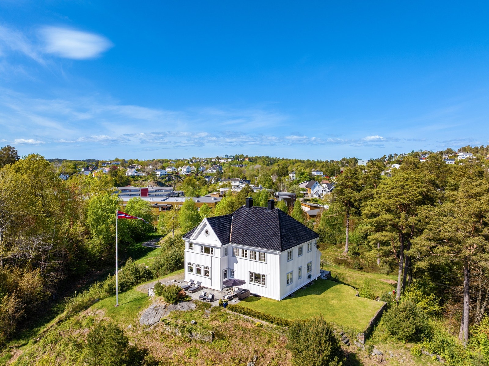 Villaen troner majestetisk på tomten, omgitt av hage, skiferkledd markterrasse og skog i bakkant. Galleribilde