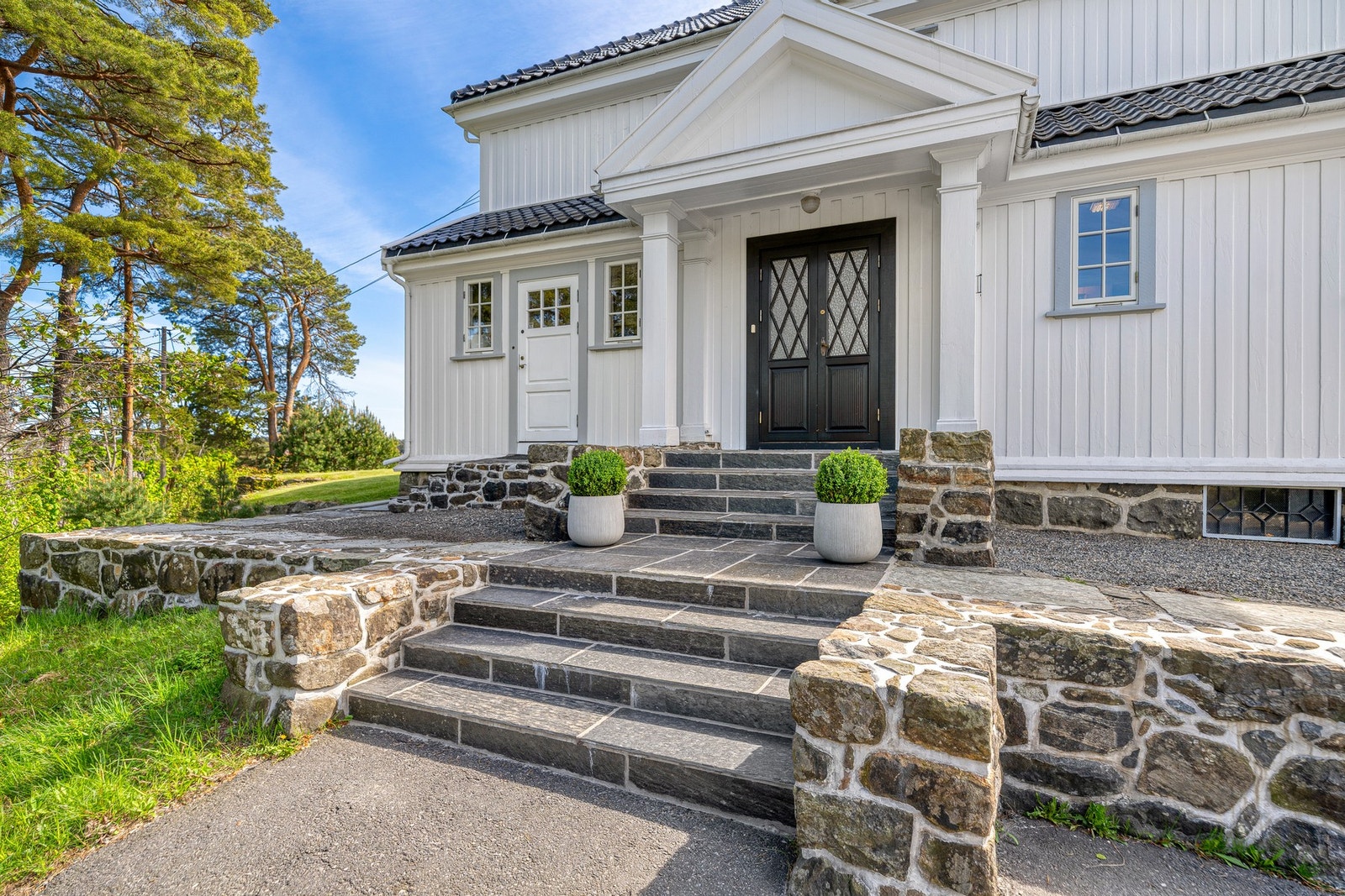 Villaen har et herskapelig inngangsparti med natursteinsterrasse, skiferkledd trapp og søyler. Galleribilde