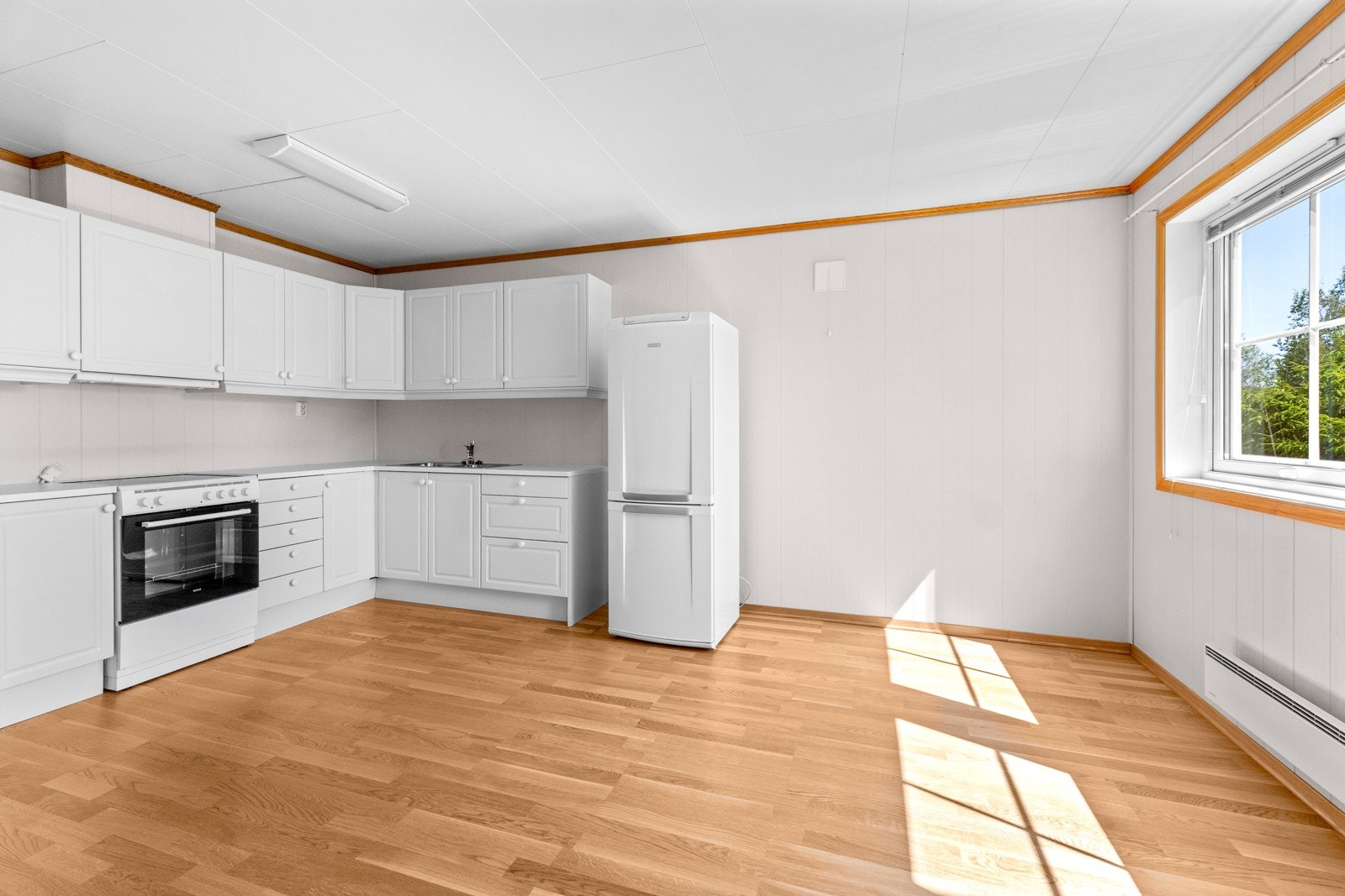 Romslig kjøkkeninnredning med hvite profilierte fronter, benkeplate av laminat og nedsenket oppvaskkum av rustfritt stål med ett-greps armatur. Galleribilde