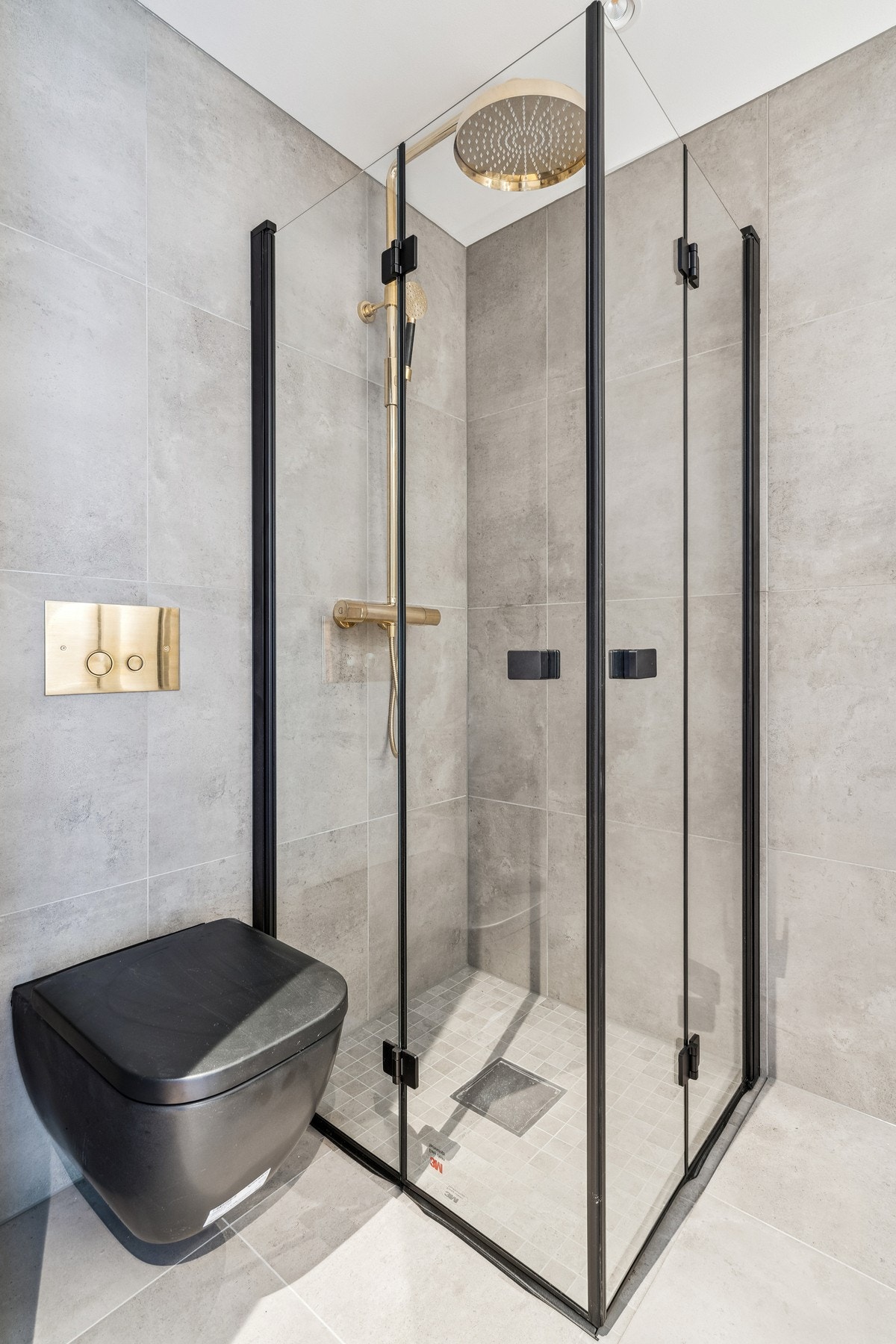 Badet er flislagt med 60x60 fliser i fargen Glade Cinza og har sort baderomsinnredning (80 cm), veggmontert toalett, håndkletørker og takdusj Galleribilde
