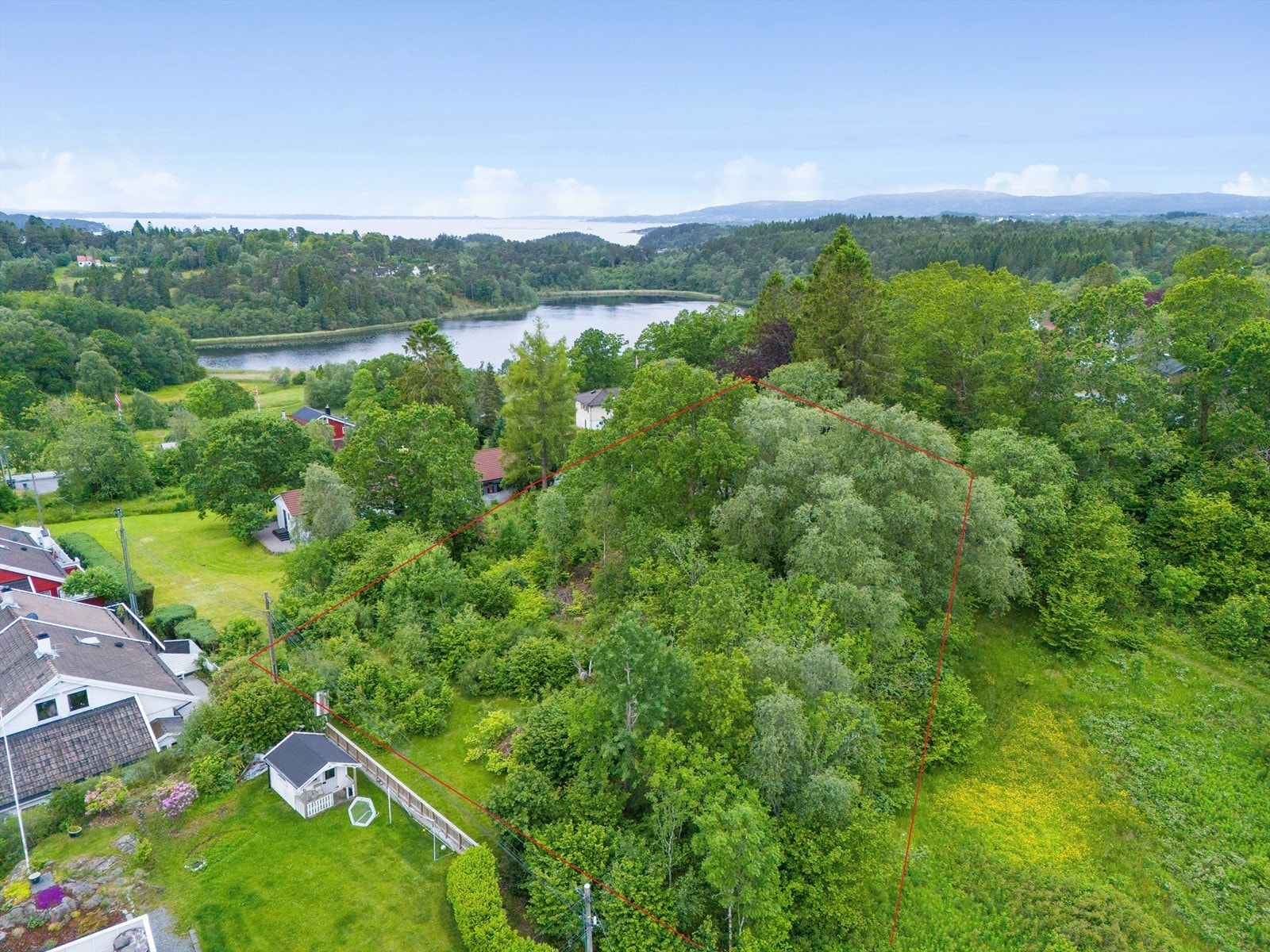 Tomten er kupert med træt og vegetasjon. Utsikt mot Mildevatnet i bakgrunnen. Galleribilde