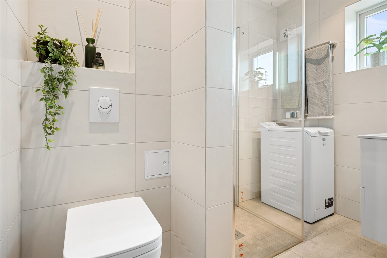 Innbydende flislagt baderom fra 2018, utført av fagfolk. Plassbesparende løsning med smal vaskemaskin ved siden av dusjhjørnet. Galleribilde
