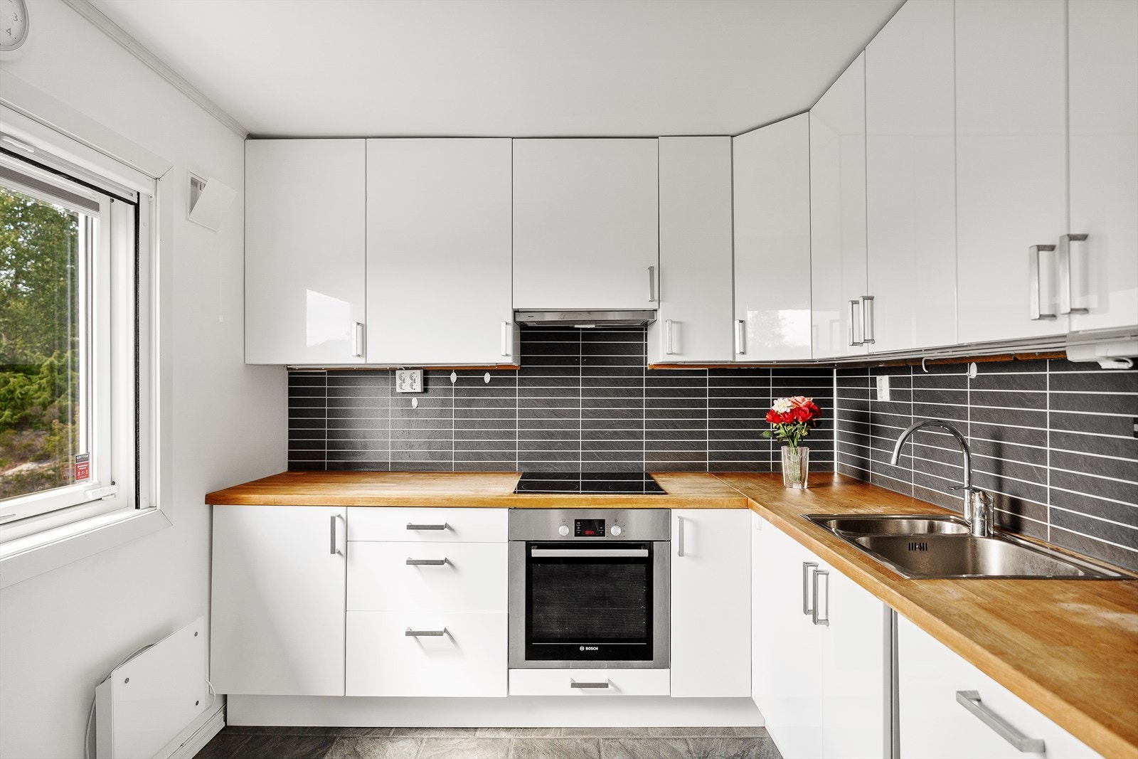 Kjøkken med kjøkkeninnredning med slette fronter, heltre benkeplate, over benkeplaten er det benyttet kitchenboard, stål oppvaskkum, ventilator. Galleribilde