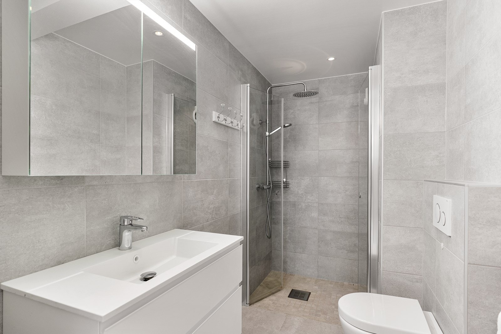 Moderne bad i 1. Etasje. Inneholder vegghengt toalett, helstøpt servant, skuffer under servant med slette fronter og dusjdører i klart glass Galleribilde