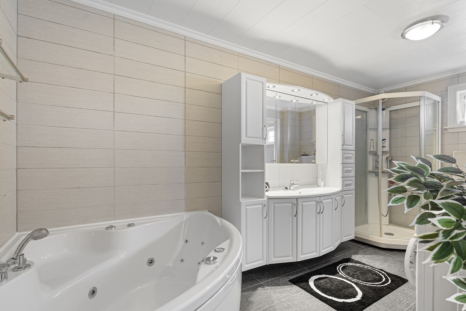 Tilleggsdel innredet som romslig bad/vaskerom. Rommet er innredet med hjørneboblekar, dusjkabinett, vegghengt toalett og baderomsinnredning med servant og speil. Opplegg for vaskemaskin. Galleribilde