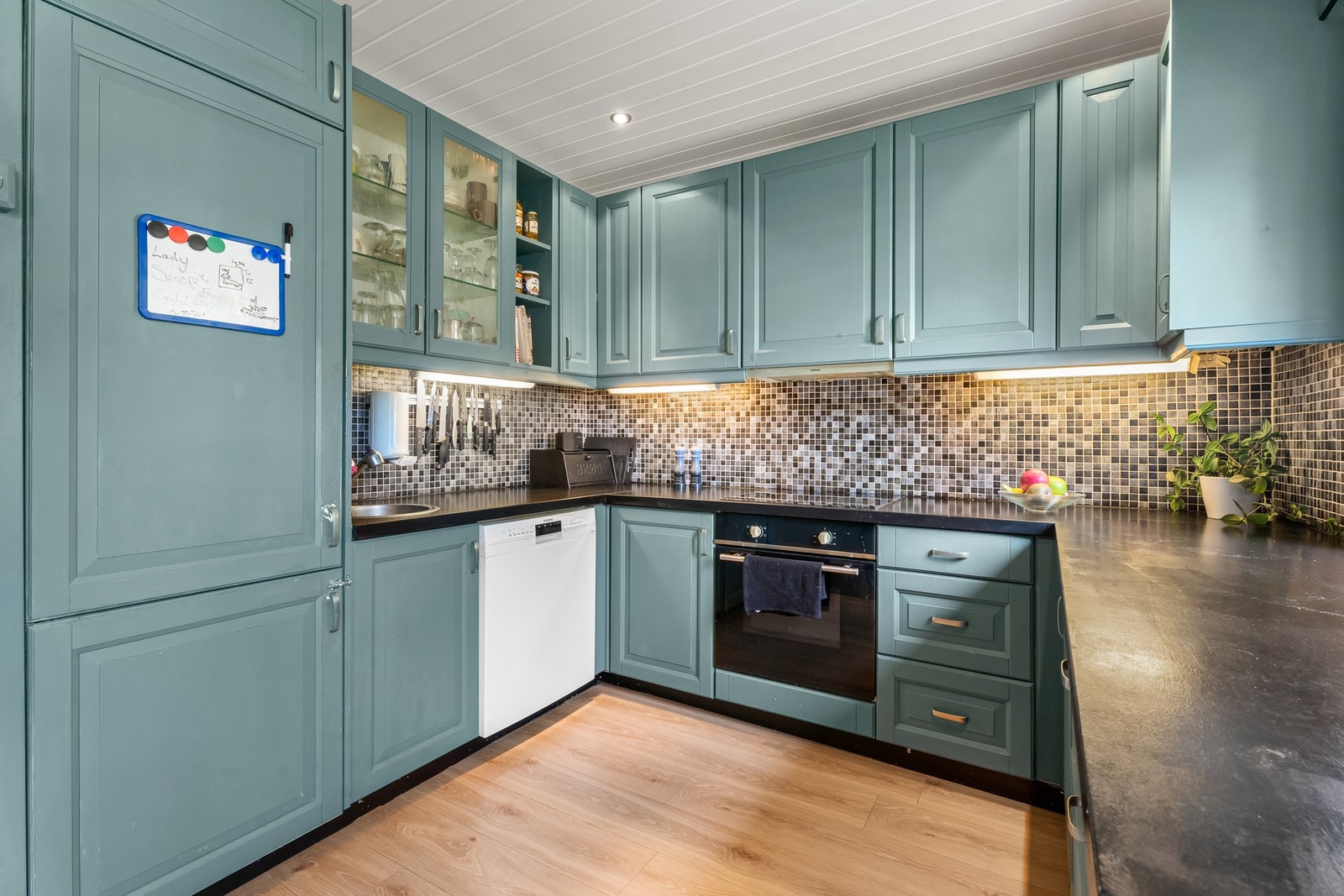 Kjøkkenet har en funksjonell utforming med god utnyttelse av plassen. Innredningen fra 2008 har malte profilerte fronter, benkeplate i malt heltre og fliser over benken som gir praktiske arbeidsflater Galleribilde