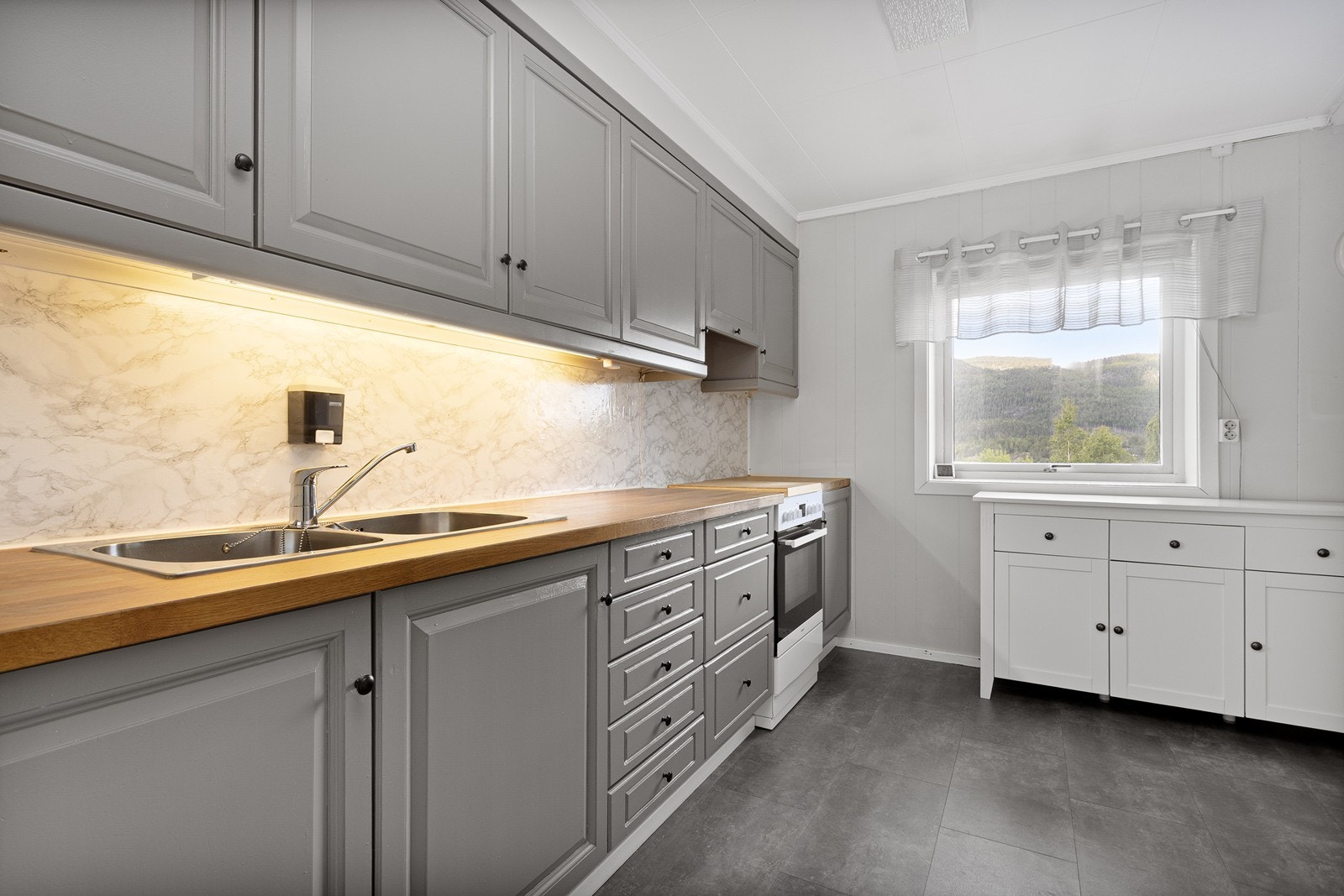 Kjøkkenet er utstyrt med en behandlet innredning med profilerte fronter og benkeplate i heltre med nedfelt oppvaskkum. Galleribilde