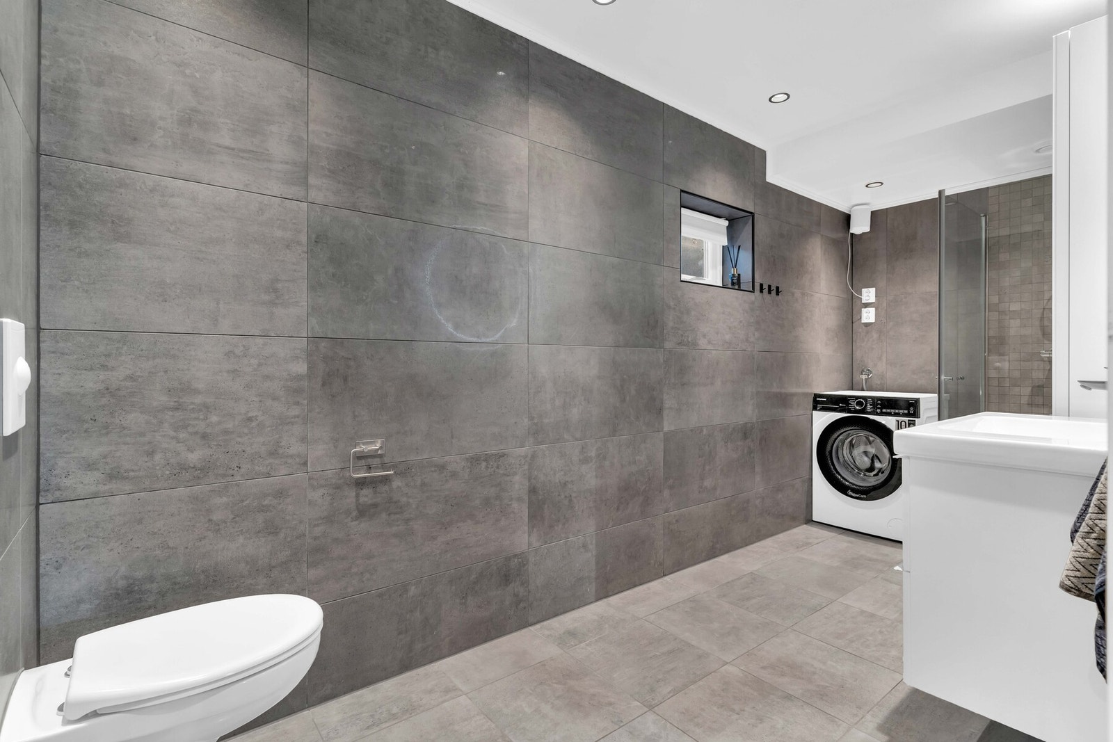 Rommet har servantskap med heldekkende servant, speil med belysning, høyskap, dusjnisje med glassdører, vegghengt toalett og opplegg for vaskemaskin/tørketrommel. Galleribilde