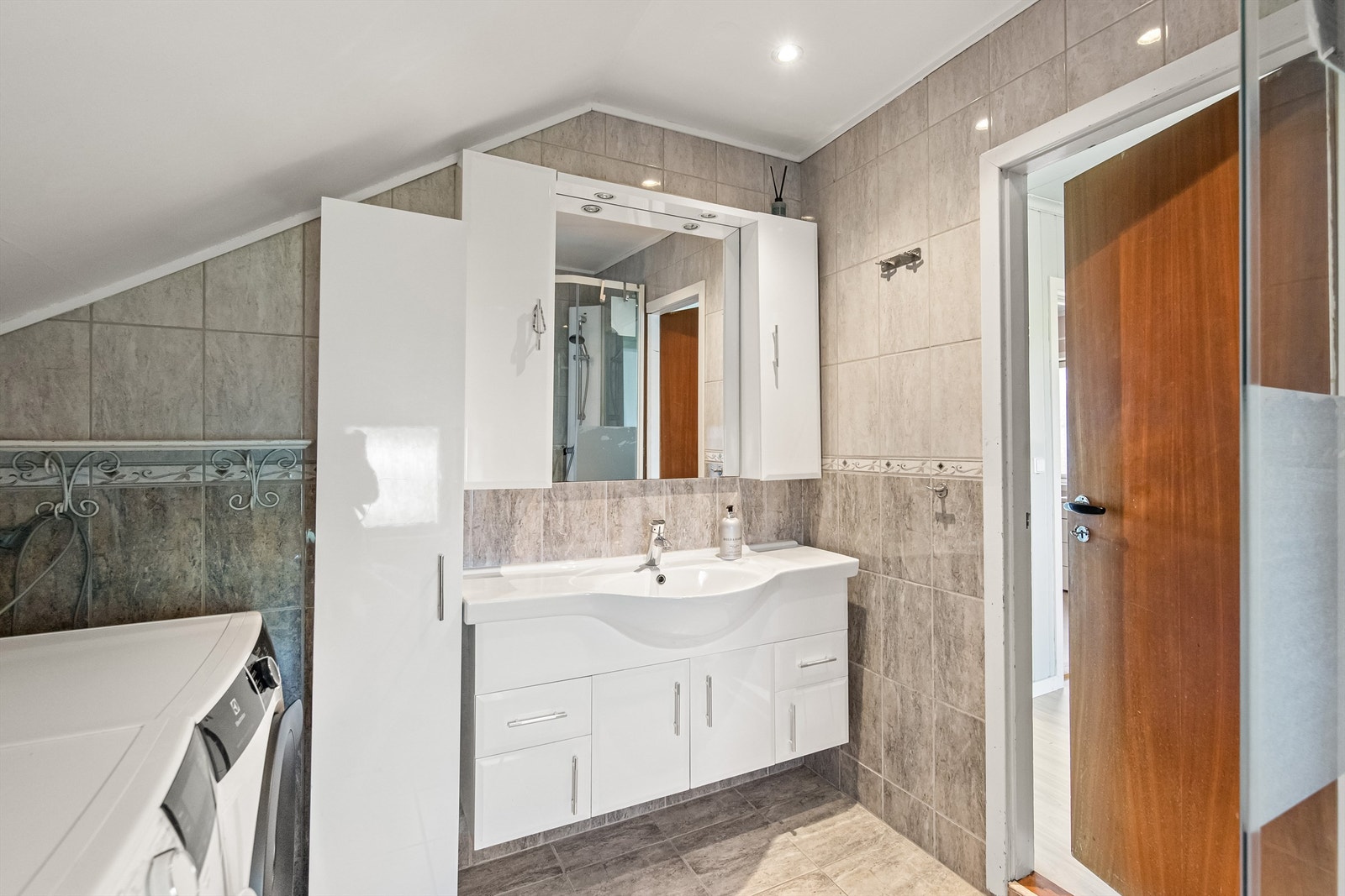 Badet er innredet med vegghengt toalett, dusjkabinett, servant i innredning og opplegg til vaskemaskin/tørketrommel Galleribilde