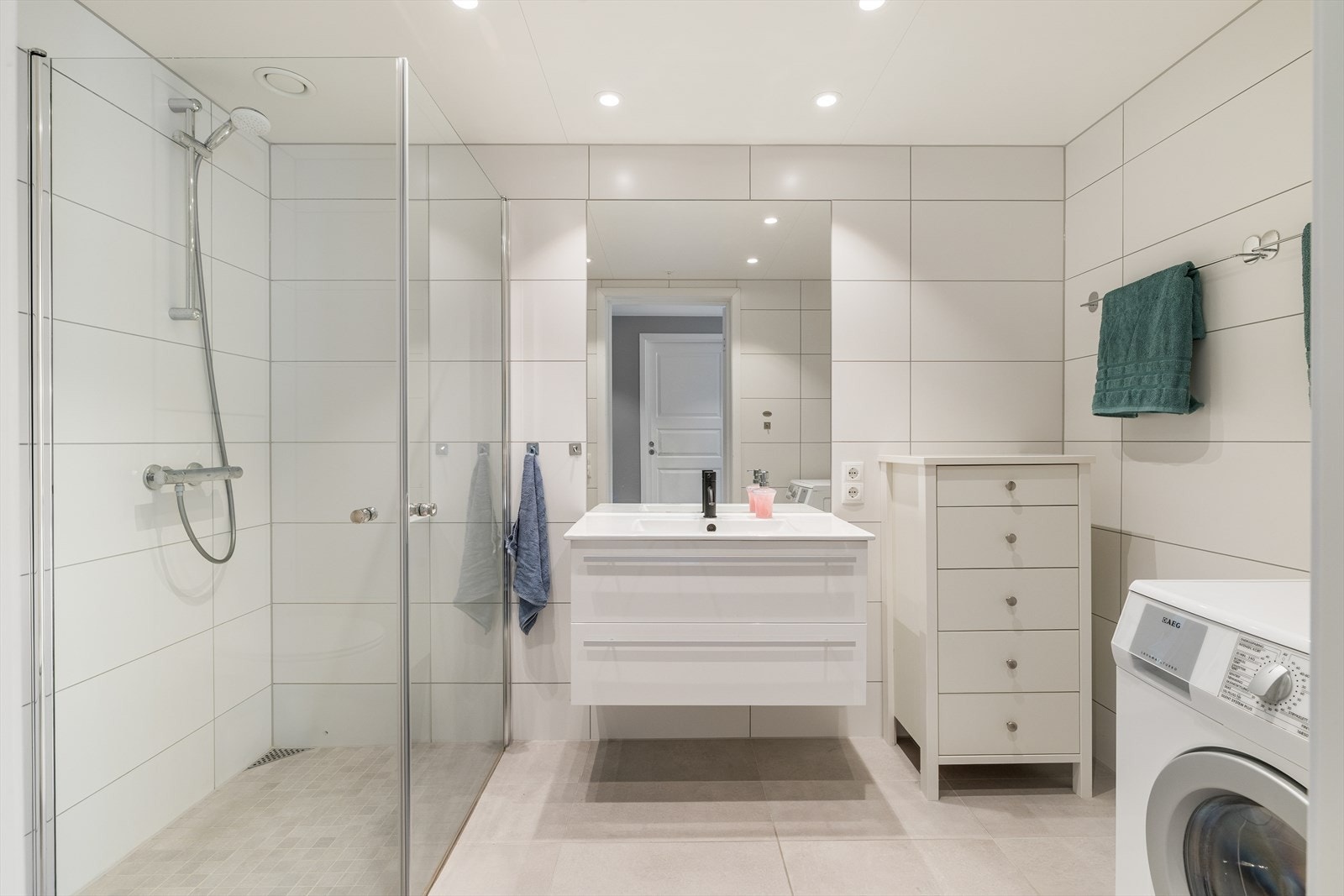 Det er et delikat baderom med tiltalende fliser på gulv og vegger. Inneholdende vegghengt toalett, innredning med servant, dusj/vegger og opplegg til vaskemaskin. Galleribilde