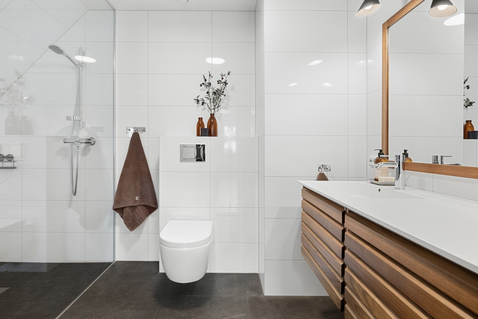 Badet er flislagt med moderne store fliser og har vegghengt toalett, dusjhjørne og servantskap med skuffer Galleribilde