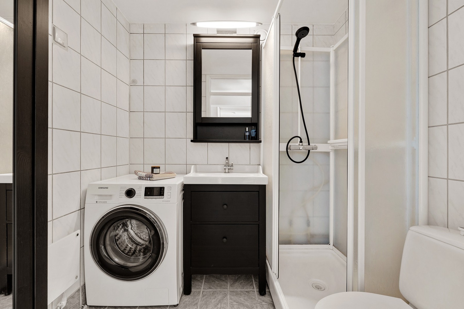 Pent flislagt bad med dusjkabinett, opplegg for vaskemaskin og oppbevaringsmuligheter i servantskap og høyskap Galleribilde