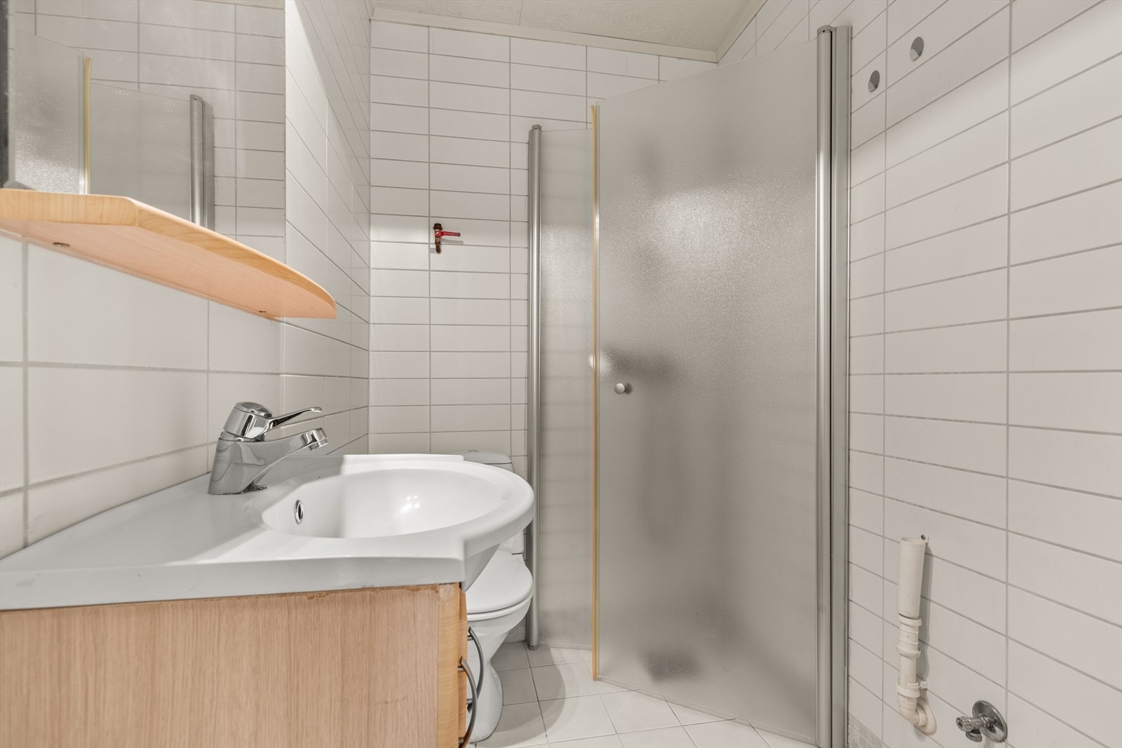 Lyst flislagt baderom med dusjnisje, servant med speil, wc og opplegg for vaskemaskin og tørketrommel. Galleribilde