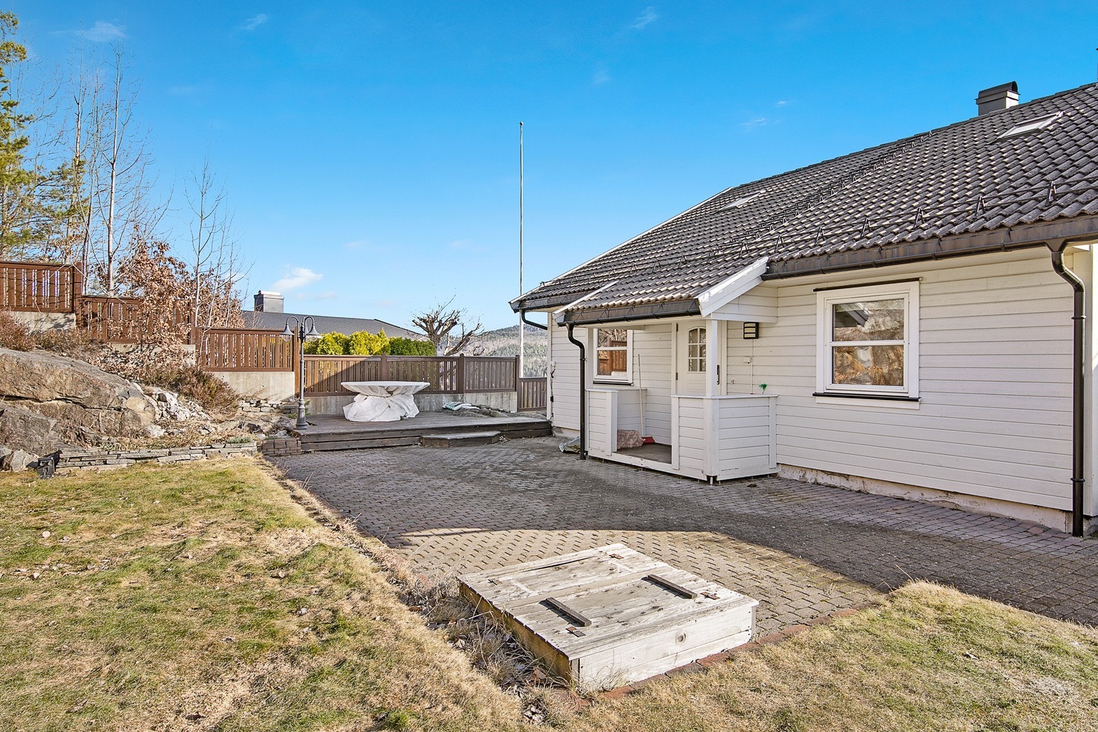 Ved inngangspartiet til leiligheten er det en koselig uteplass opparbeidet med terrasse, belegningsstein, gressplen og bedd med beplantning. Galleribilde