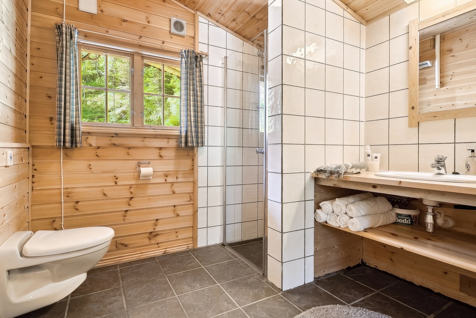 Badet har plassbygd innreiing i heiltre, vegghengt jetstoalett og dusjnisje med glasvegg. Galleribilde