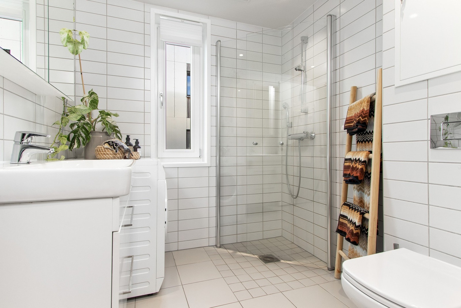 Baderommet har en nøytral stil med hvite fliser på veggene og grå fliser med varmekabler. Galleribilde