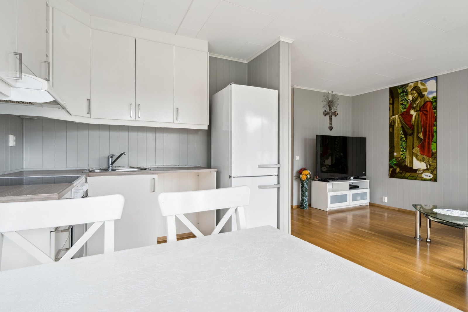 Benkeplater er av laminat, det er nedfelt oppvaskkum med ettgreps armatur, benkeskapsbelysning og stikkontakter under overskap, frittstående kjøleskap med fryserdel, og innfelt komfyr med keramisk platetopp Galleribilde