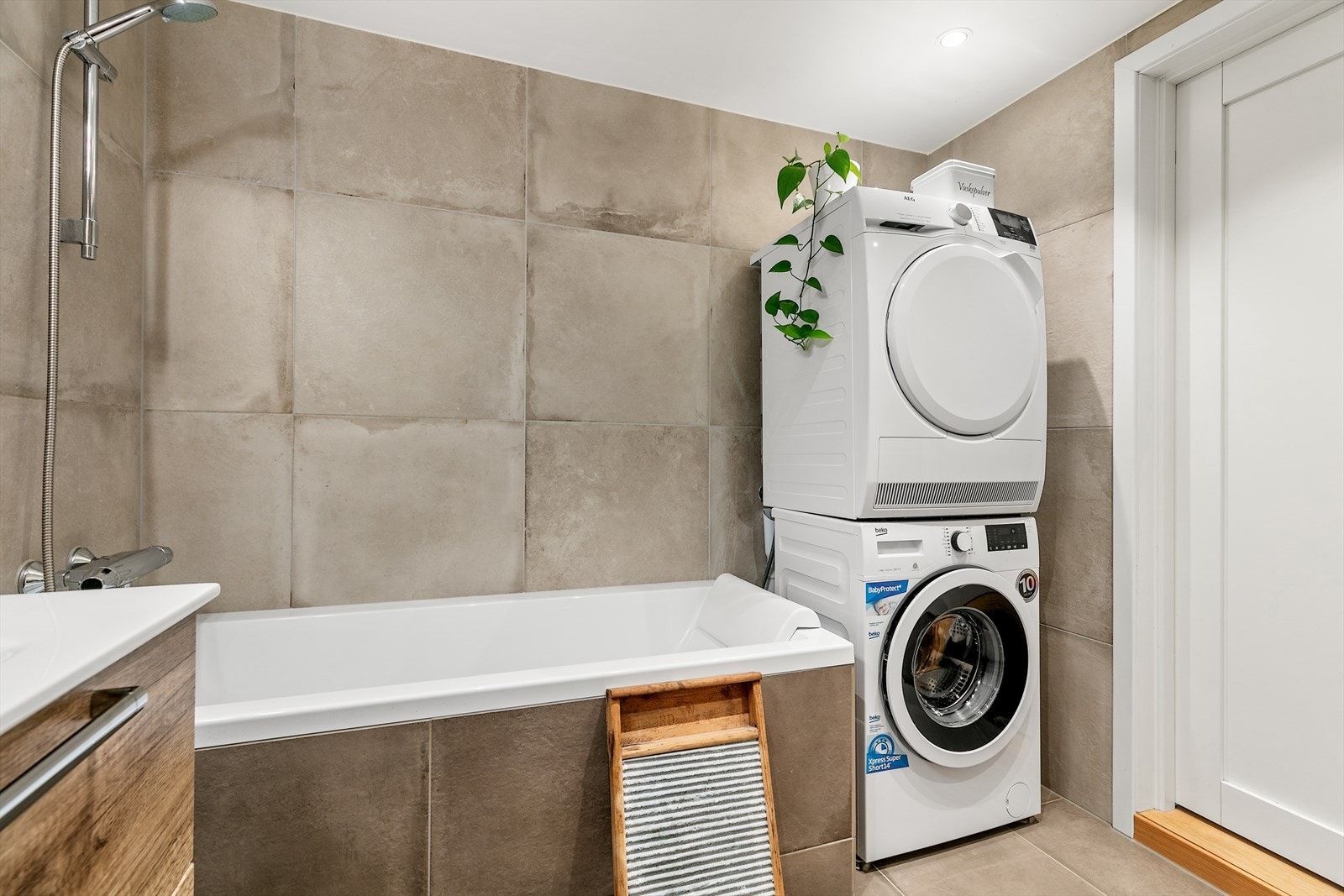 Baderomsinnredningen består av vegghengt toalett, servant med underskuffer, speil, veggskap, badekar med dusj, og opplegg for vaskesøyle i hjørne Galleribilde