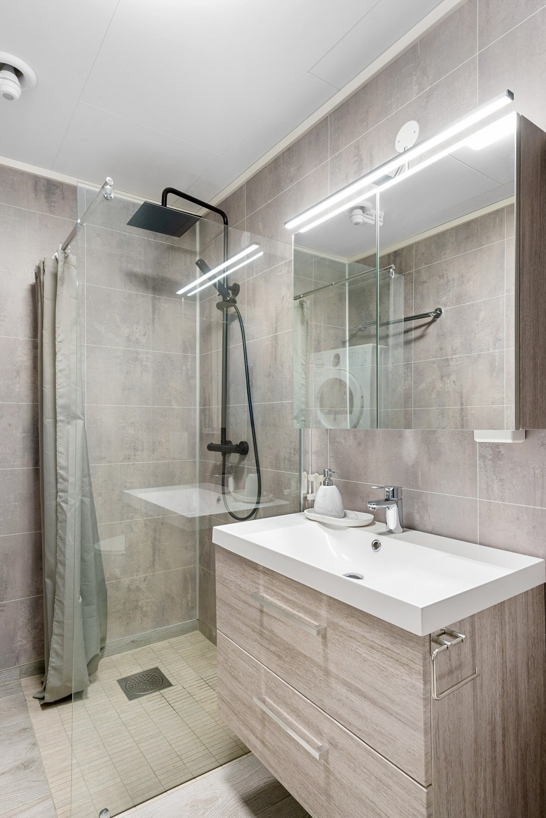 Badet har servantinnredning med skuffer, speilskap m/lys, dusjnisje med glassvegg og vegghengt armatur med både hånddusj og regndusj. Vegghengt toalett. Det er opplegg for vaskemaskin. Galleribilde