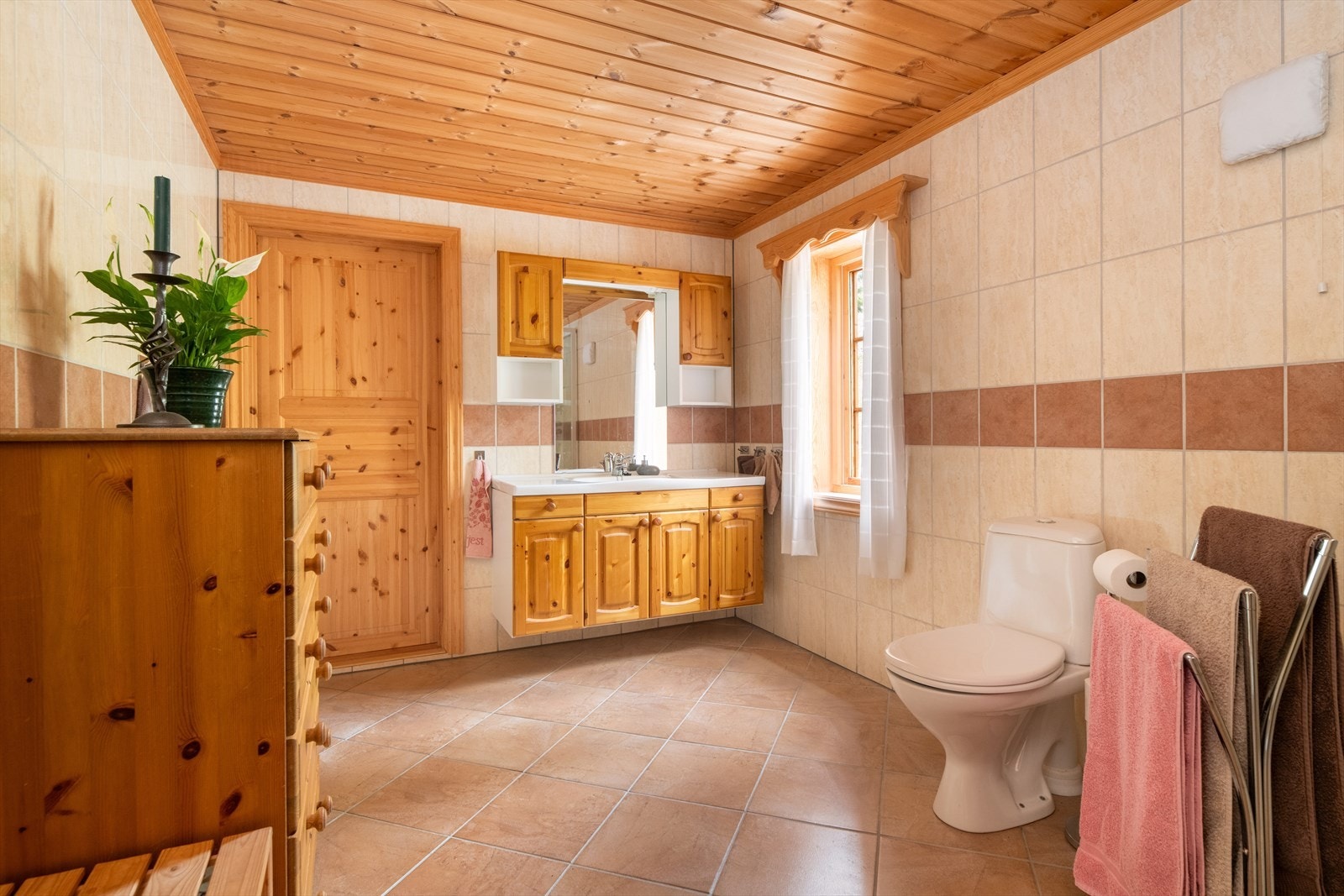 Hytta har et stort bad som er helfliset med varmekabler i gulvet. Her er en baderomsinnredning med fronter av patinert furu, med heldekkende servant og speil med overlys og el-stikk. Galleribilde