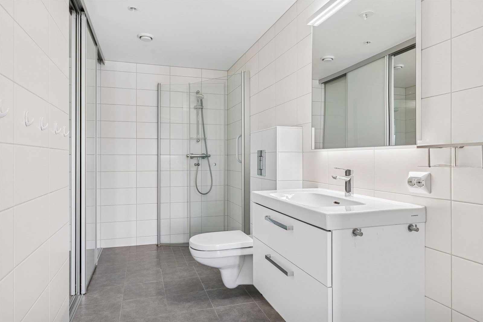 Tidløst bad med flislagt gulv og vegger, samt vannbåren gulvvarme til oppvarming. Badet er utstyrt med vegghengt toalett og servantskap, dusjnisje med glassdører, vaskemaskin og vannfordelerskap. Galleribilde