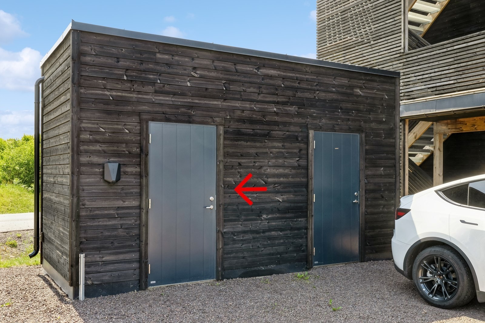 Utvendig sportsbod med biloppstillingsplass utenfor boden og elbillader. Galleribilde